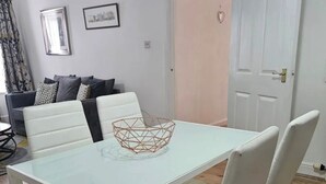Un coin repas avec une table blanche, quatre chaises blanches et un bol en métal aux motifs géométriques posé sur la table.