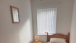 Une chambre à coucher avec un lit en bois, une table de chevet avec une lampe, une fenêtre avec des stores et un miroir au mur.