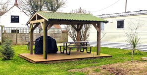 A wooden gazebo with a metal roof, a picnic table, and a barbecue grill in a backyard. - Fieldview Lodge Dog Friendly nr Sutton on Sea (Alford)