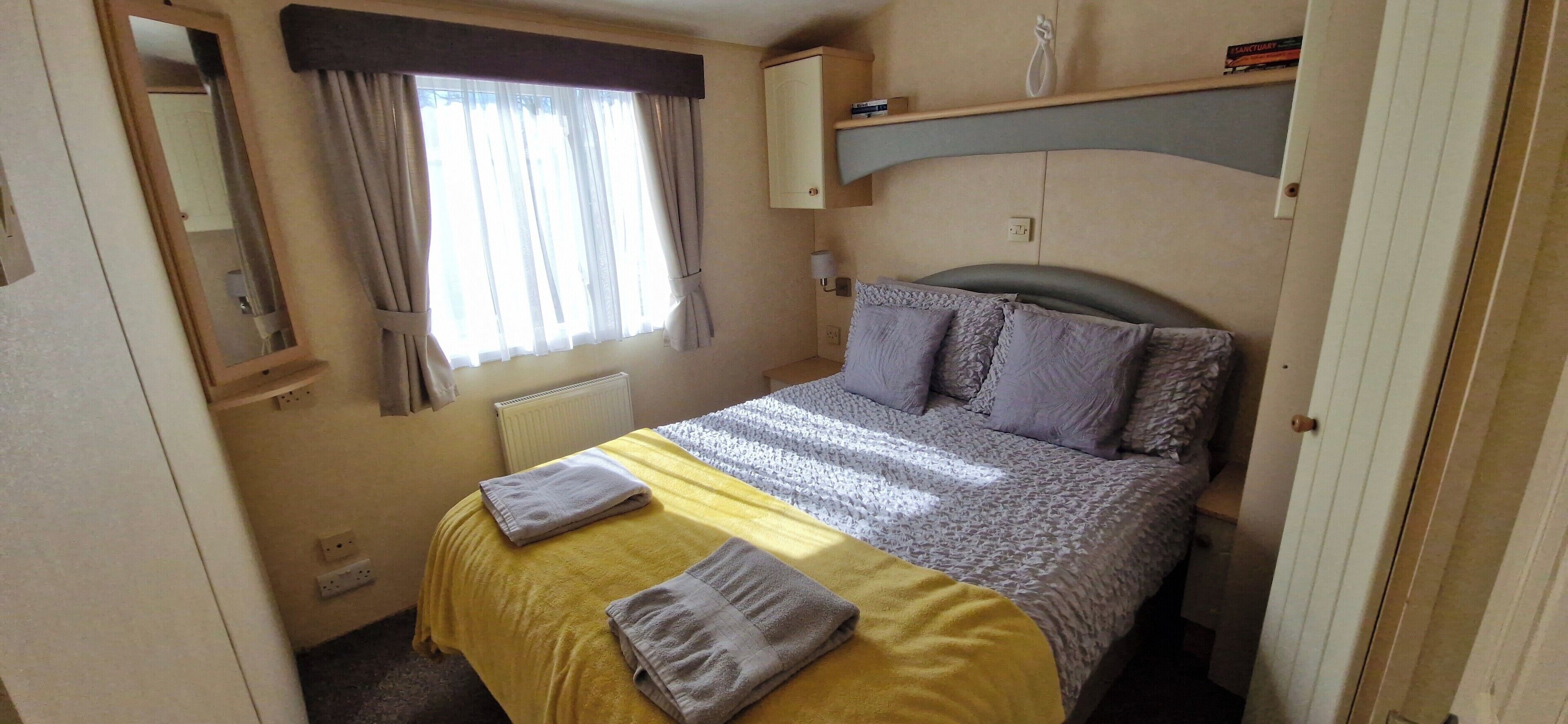 A bedroom with a bed, a window with curtains, a bedside table, and a mirror.