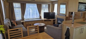 A compact RV interior with a seating area, a television, a small table, and a kitchenette. - Fieldview Lodge Dog Friendly nr Anderby Creek (Alford)