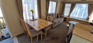 A cozy living area with a wooden dining table, cushioned chairs, a sofa, and a window with curtains. - Fieldview Lodge Dog Friendly nr Anderby Creek (Alford)