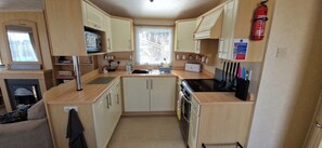 A compact kitchen with a sink, stove, microwave, and cabinets. - Fieldview Lodge Dog Friendly nr Sutton on Sea (Alford)