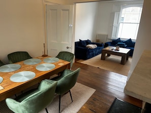 Une salle à manger avec une table en bois et des chaises vertes, un salon avec un canapé bleu et une table basse, et une porte blanche.