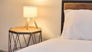 A bed with white bedding, a round wooden nightstand with a lamp, and a wooden headboard. - Apartment Sleeps 8 with WiFi (Nottingham)