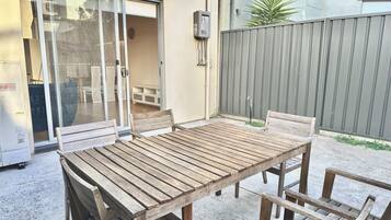 An outdoor patio with a wooden table and chairs, a sliding glass door, and a grey fence.