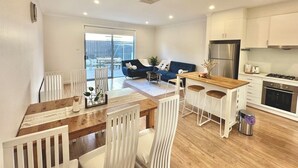 A modern kitchen with white cabinets, a wooden dining table, and a bar area.