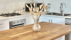 A kitchen with white cabinets, a wooden countertop, a vase with dried plants, and a stove.