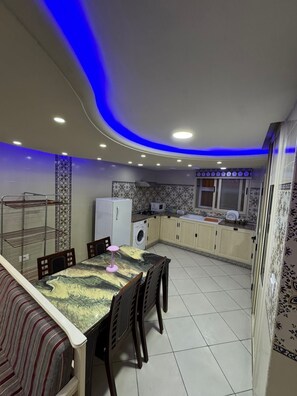 A modern kitchen with a dining area, featuring a curved ceiling with blue lighting, a washing machine, and a microwave. - Duplex in the Heart of the Medina (Kairouan)