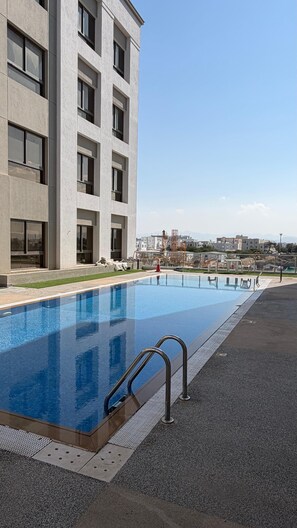 Un bâtiment moderne doté d’une piscine, avec un ciel dégagé et un chantier de construction visible au loin.