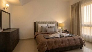 Ein Hotelzimmer mit einem großen Bett, einem Schminktisch, einem Nachttisch mit Lampe und einem Fenster mit Vorhängen.