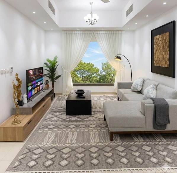 Un salon moderne avec un téléviseur à écran plat, un canapé, une table basse et un tapis à motifs.