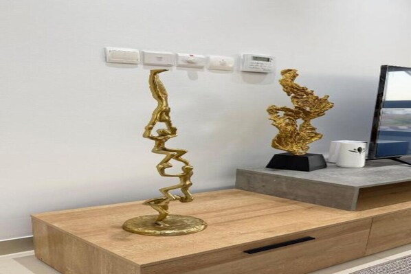 Une pièce moderne avec une console en bois, une sculpture abstraite dorée et un téléviseur à écran plat posé sur un meuble.