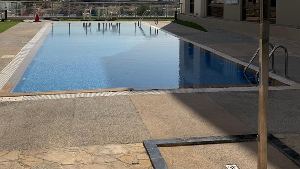 Ein Pool mit Steinbord, einer Metallleiter und einem Gebäude mit mehreren Fenstern im Hintergrund.