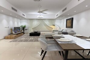 A modern living room with a dining area, a sofa set, a flat-screen TV, and a ceiling fan. - Perfect choice Apartment-AlMuzn Residence, AirPort (Seeb)