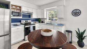 Une cuisine moderne avec des meubles blancs, des appareils en acier inoxydable, une table ronde en bois et une plante en pot.