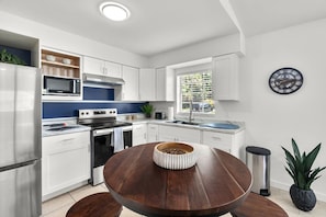 Eine moderne Küche mit weißen Schränken, Edelstahlgeräten, einem runden Holztisch und einem Blumentopf.