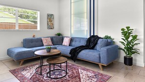 Un salon moderne avec un canapé d’angle, une petite table basse ronde, un tapis à motifs et une plante en pot.