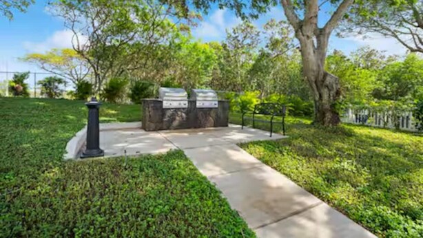 A paved pathway leading to a barbecue area with two grills, surrounded by lush greenery and trees. - Aloha Kai | AC | Pool & Hot Tub | Beach Access (Koloa)
