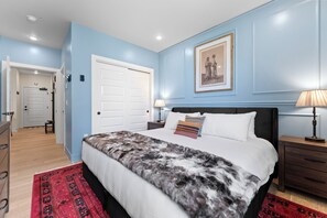 Une chambre à coucher avec un lit, des tables de chevet, une lampe, une porte et un couloir.
