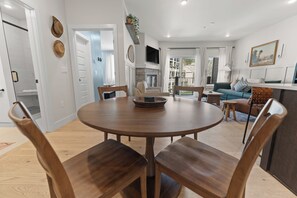 A modern living room with a round wooden dining table, two wooden chairs, a sofa, and a TV mounted on the wall. - New Designer Condo-King Bed, Pool/HT, Spa, Lake (Keystone)