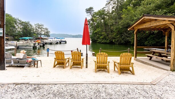 Terraza junto al lago con sillas Adirondack, una sombrilla roja y un pabellón de madera.