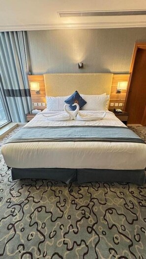 A hotel room with a large bed, a headboard, two bedside tables, a window with curtains, and a patterned carpet. - AL Shahba AL Faiha Hotel (Jeddah)