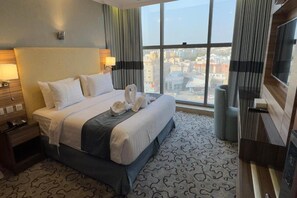 Una habitación de hotel con una cama grande, televisión, vistas a la ciudad y alfombra estampada.