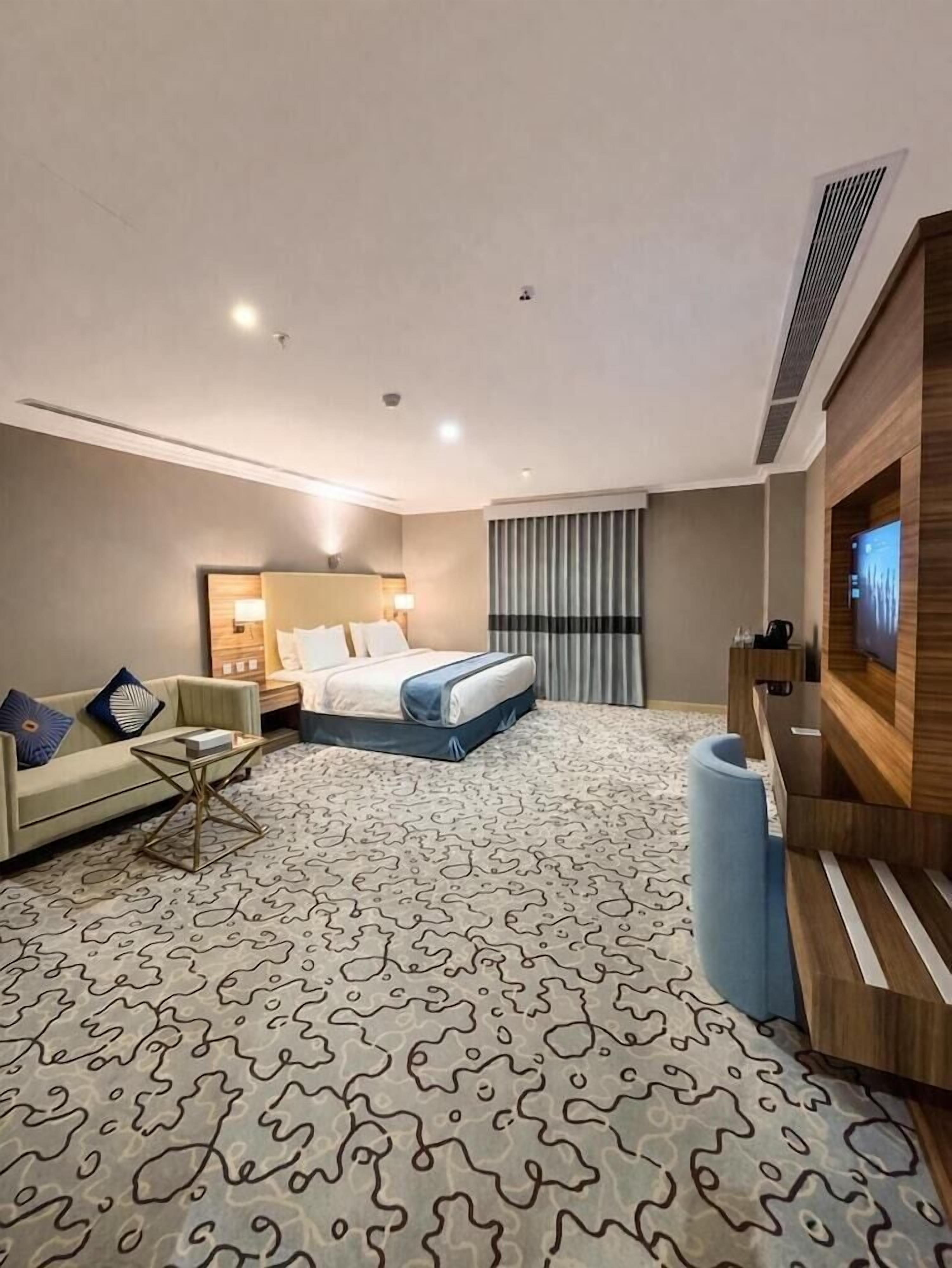 Una habitación de hotel con cama, sofá, televisión y alfombra estampada.