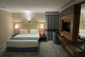 Una habitación de hotel con una cama grande, lámparas de noche, televisión, espejo y alfombra estampada.