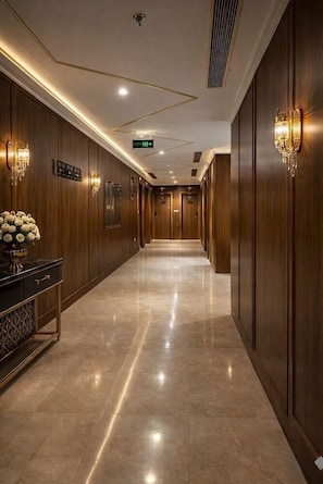 A hotel corridor with wooden paneling, marble flooring, wall sconces, and a directional sign. - AL Shahba AL Faiha Hotel (Jeddah)