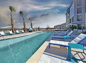 Ein Pool mit Liegestühlen, Palmen und ein Gebäude mit dem Schild 'NOW LEASING'.