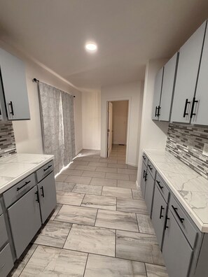 A modern kitchen with grey cabinets, marble countertops, and a tiled floor.