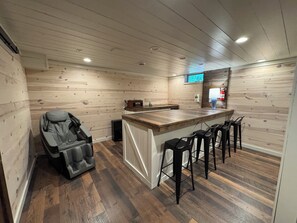 Un cuarto de spa con una silla de masaje, una barra de madera con taburetes y un televisor en la pared.