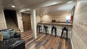Eine moderne Küche mit einer Holztresore und Barhocker, einer Treppe, die zu einem Schlafzimmer führt, und einem Ledersofa mit Kissen.