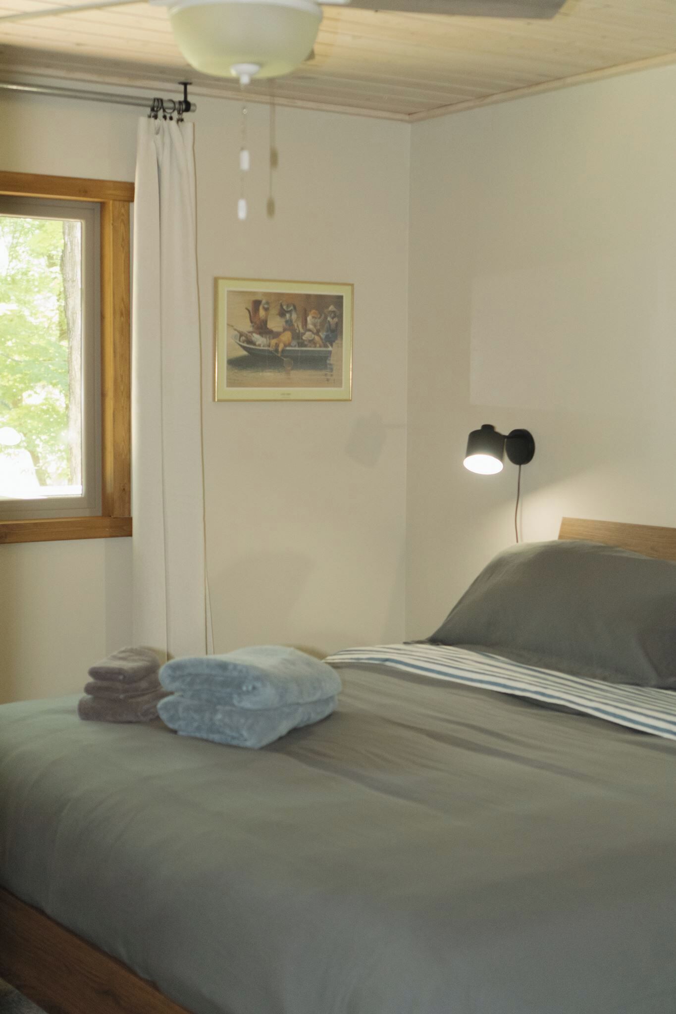 Um quarto com uma cama, uma janela com cortinas, um quadro na parede e um abajur.