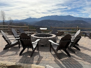 A fire pit surrounded by Adirondack chairs on a brick patio with a mountain view. - 4th July Family Vacation 4-bedroom Resort Cabin with Mountain view & Water Park (Gatlinburg)