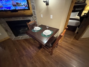 A dining area with a wooden table set for two, a stone fireplace, and a television mounted on the wall. - 4th July Family Vacation 4-bedroom Resort Cabin with Mountain view & Water Park (Gatlinburg)