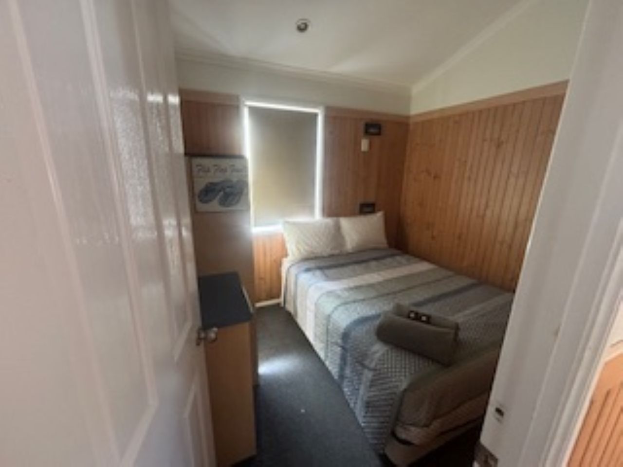 Quarto compacto com cama, escrivaninha pequena e janela.