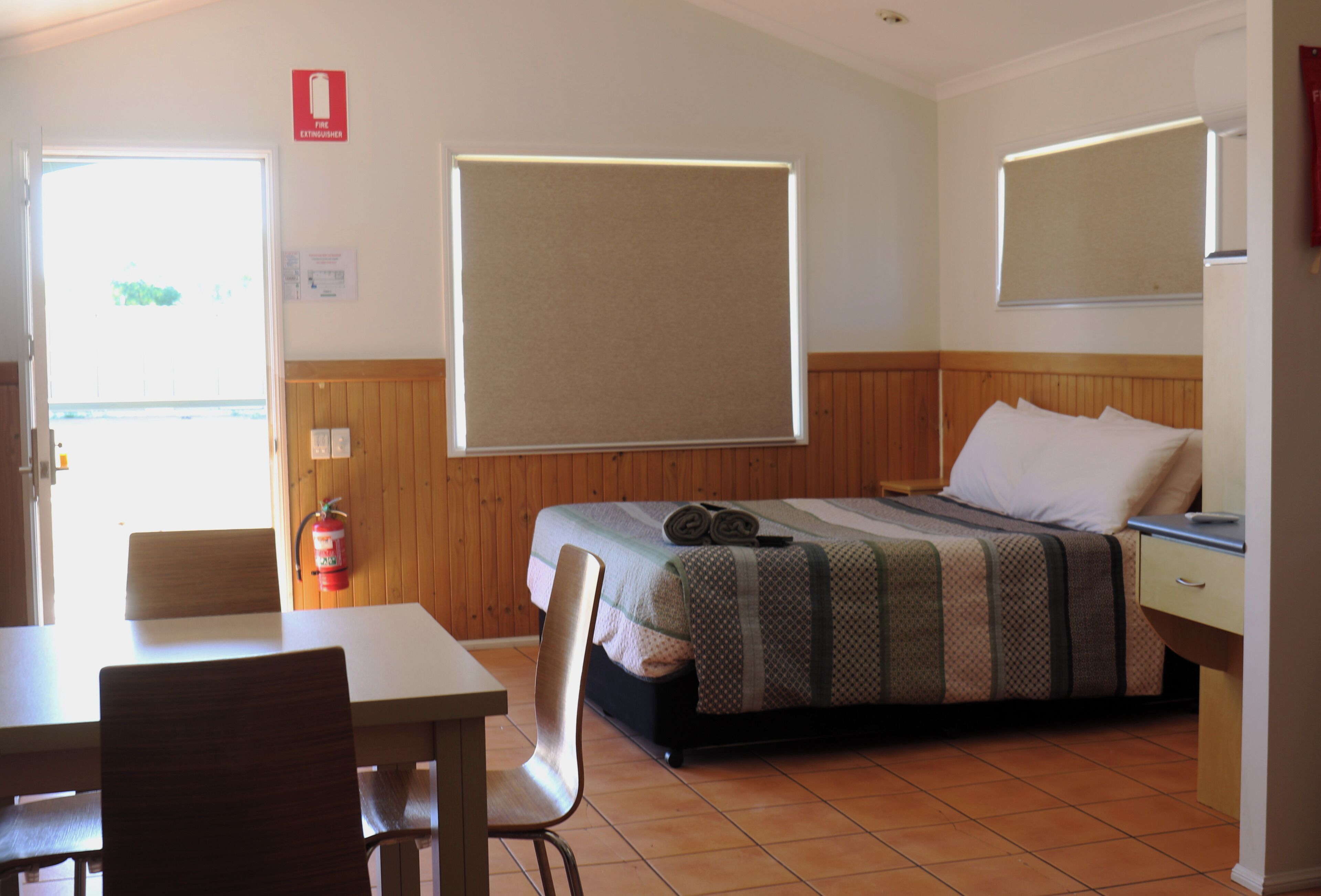 Quarto com uma cama, uma mesa, uma cadeira, uma janela e um extintor de incêndio.