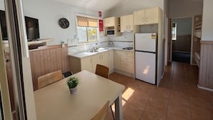 A compact kitchen with a dining table, a refrigerator, and a microwave. - Longreach Starlight Cabins (Longreach)