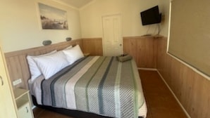 A bedroom with a bed, a television mounted on the wall, and a door. - Longreach Starlight Cabins (Longreach)