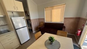 A compact kitchen with a refrigerator, a dining table with chairs, and a small plant on the table. - Longreach Starlight Cabins (Longreach)