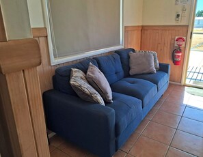 Um sofá azul com várias almofadas em um quarto com painéis de madeira e piso de azulejos.
