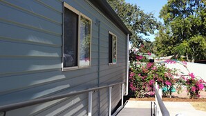 A grey mobile home with a wooden deck and a metal railing. - Longreach Starlight Cabins (Longreach)