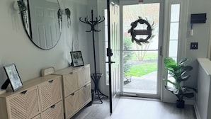 Ein Flur mit einem Holzschrank, einem Spiegel, einem Kleiderhaken und einer zur Außenwelt führenden Tür.