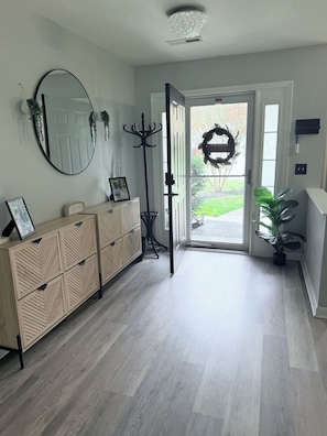 Un couloir avec une armoire en bois, un miroir, un porte-manteau et une porte donnant sur l’extérieur.