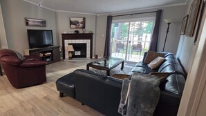 Ein Wohnzimmer mit Fernseher, Kamin, Ledersofa und Glastisch.