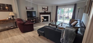 A living room with a TV, fireplace, leather sofa, and a glass coffee table. - Sunset Cove - Serene Lake Hartwell Lakefront Escape (Fair Play)