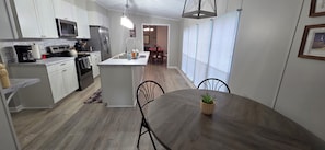 A modern kitchen with white cabinets, a central island, and a dining area with a table and chairs. - Sunset Cove - Serene Lake Hartwell Lakefront Escape (Fair Play)